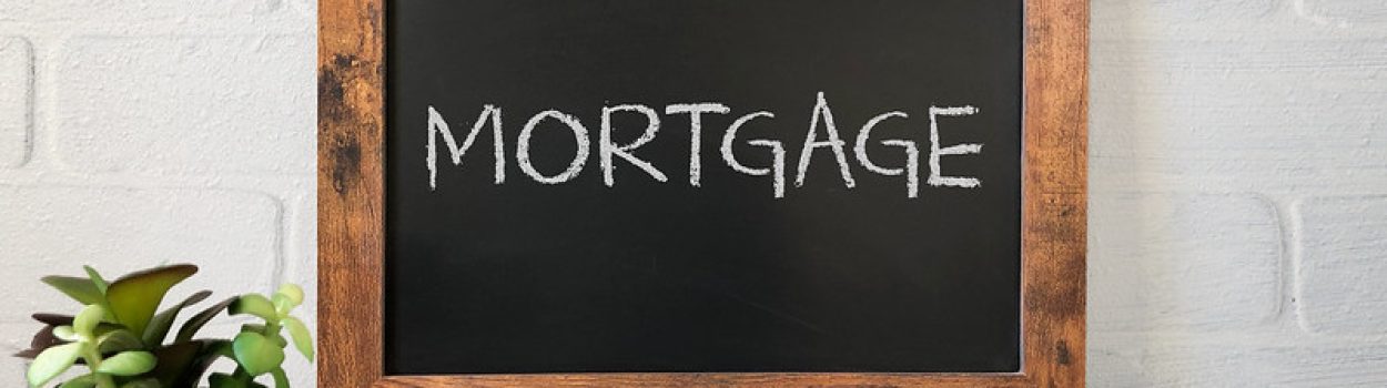 How to Find a Great Lender plant, pens, binder clips and calculator on desk with chalkboard sign saying 'Mortgage'